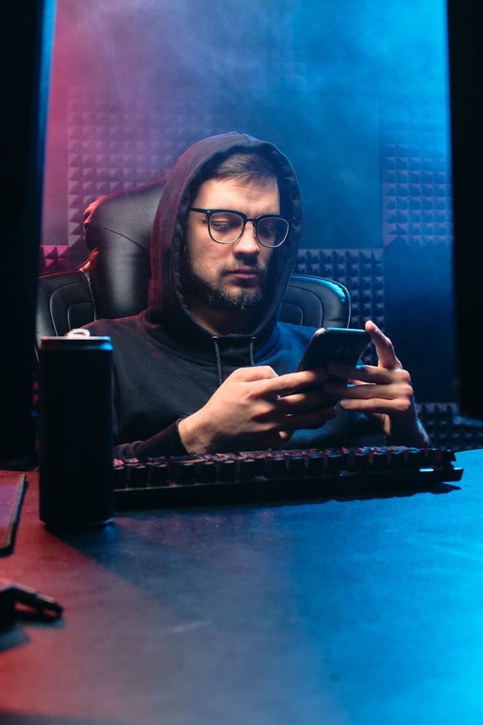 Man in dark office using smartphone, embodying cyber and tech themes.